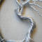 Detailed wire art featues a silver tree with twisted roots and branches inside a circular rustic frame extreme cloesup